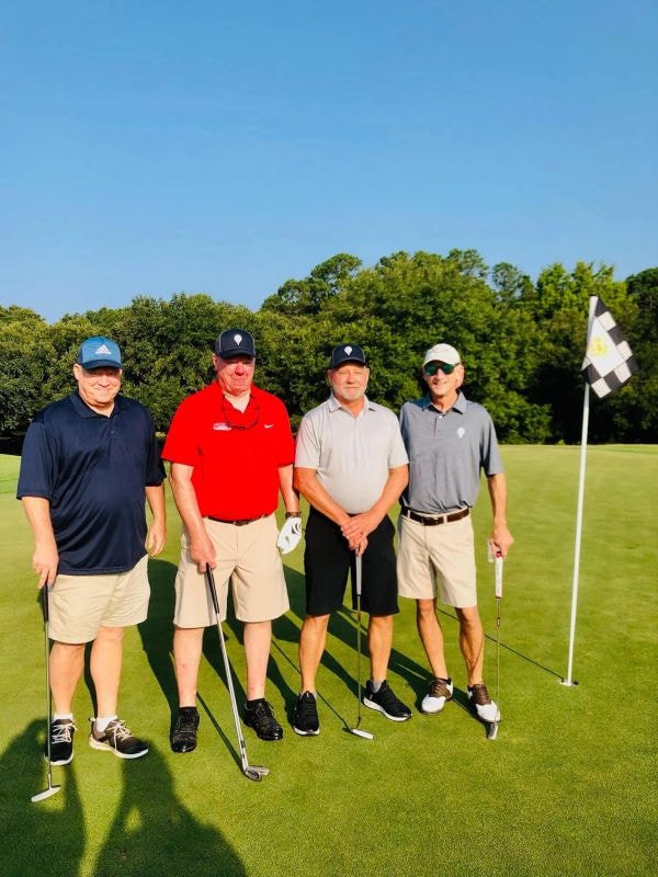 Four golfers posing on the green by the flag