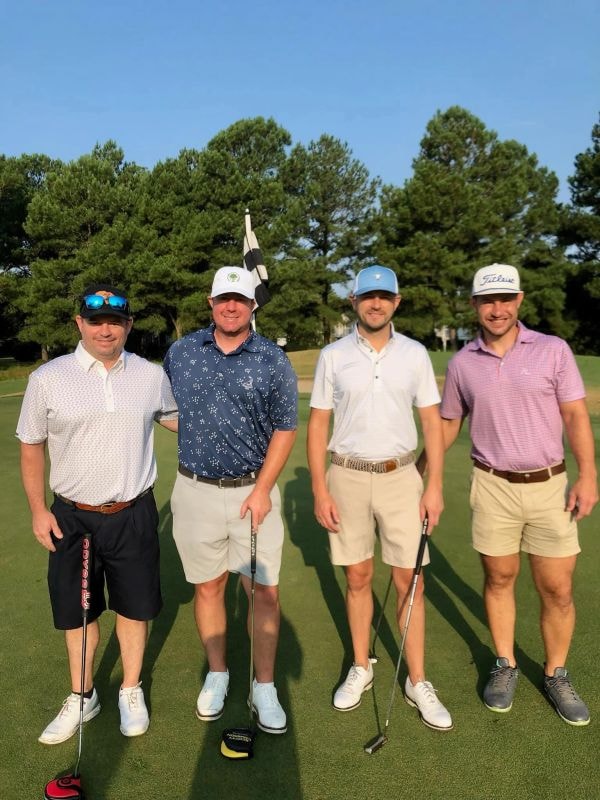 Four golfers posing on the green with flag