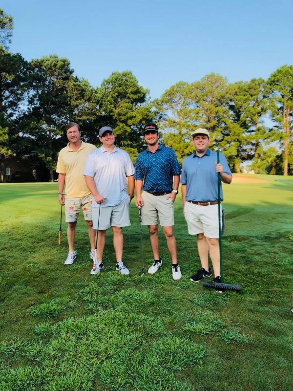 Four men posing on sunny golf course green